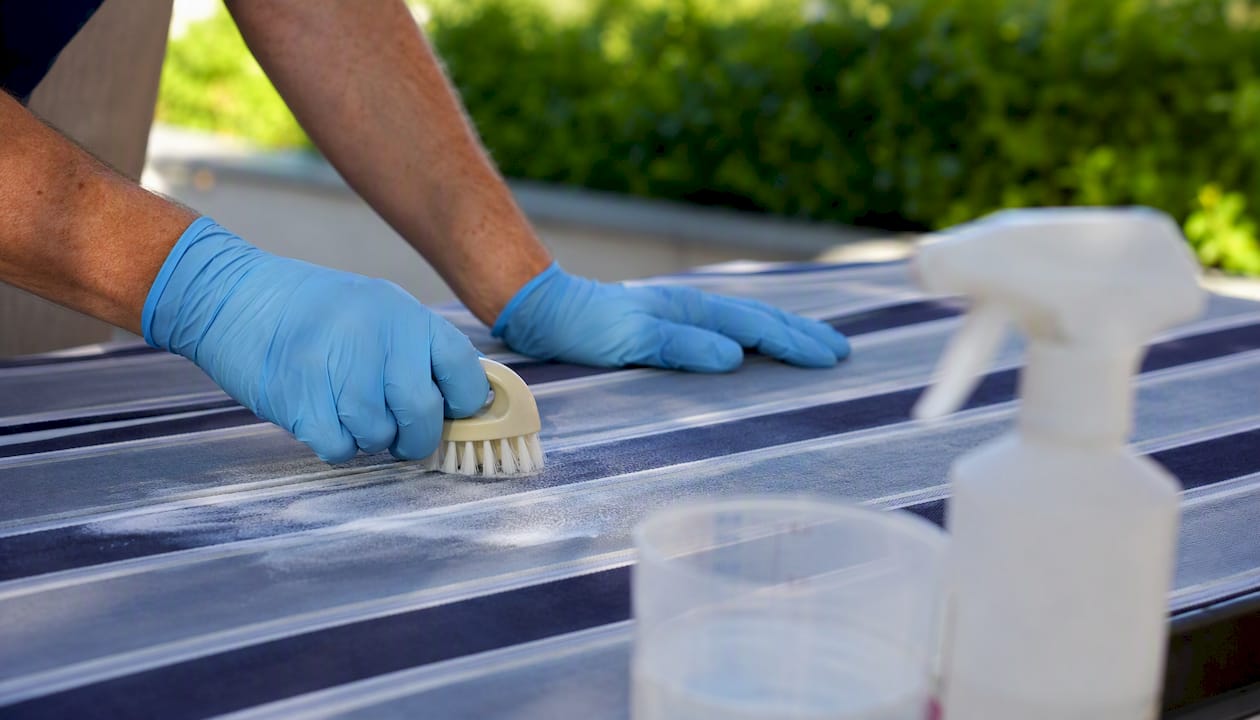 Hands applying diluted bleach on awning fabric section