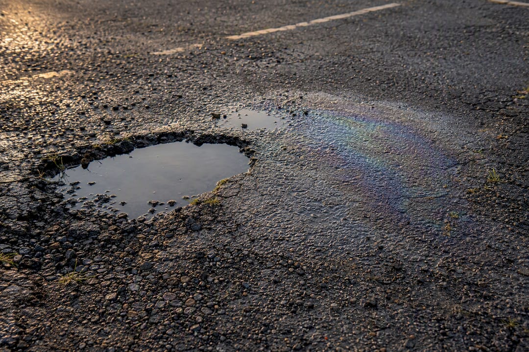 Close-up of pothole, oil stain, and gravel on parking lot