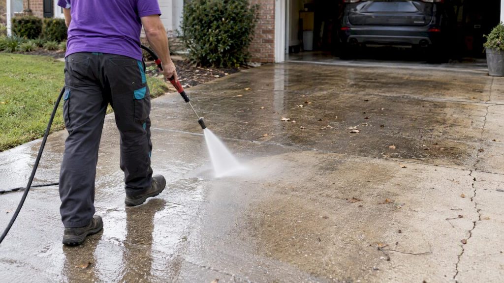 Operator pressure washing stained concrete driveway