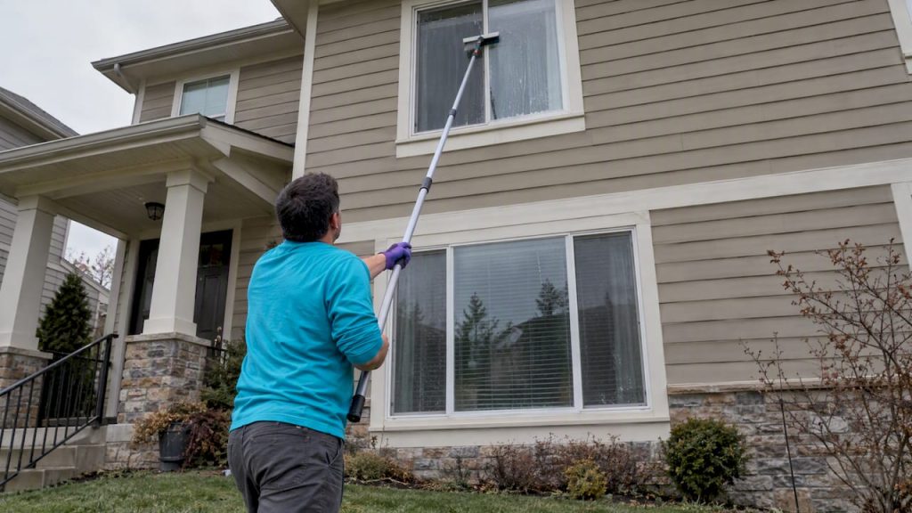 Homeowner cleaning an upper window from the ground